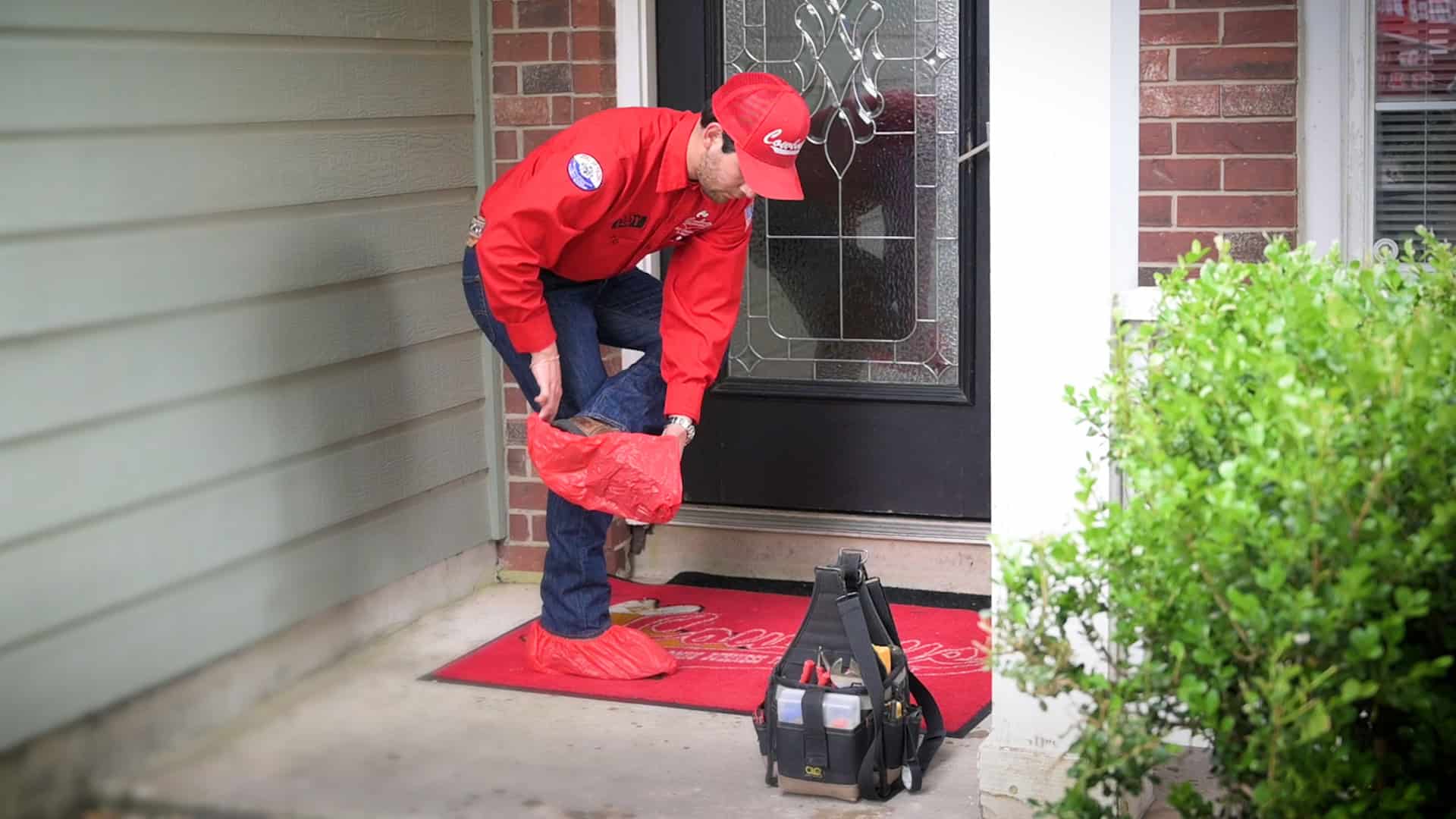 A Cowboy's technician pulling shoe covers on at a customer's front door